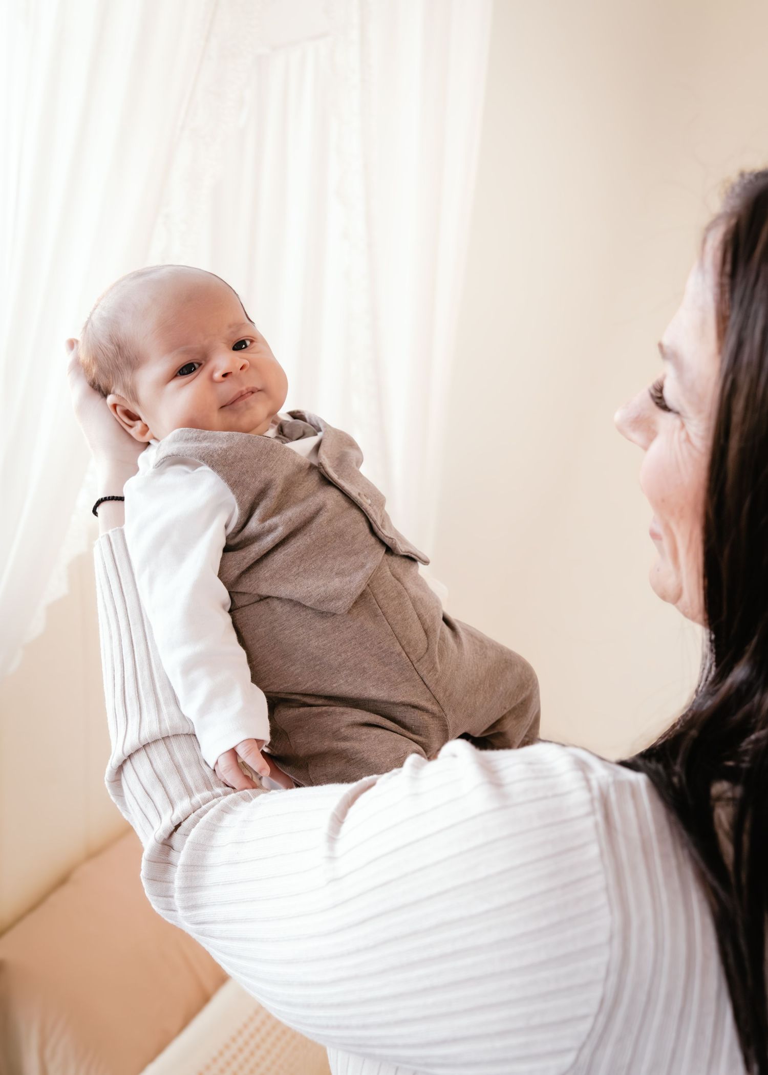 Parent holds and lifts a baby wearing a gray onesie in a series of gentle movements against a light background.