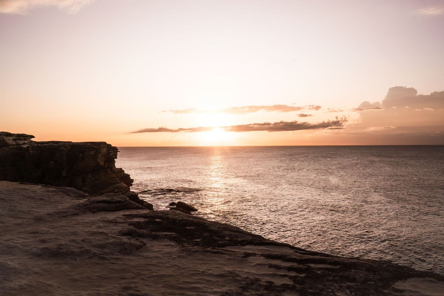 Dramatic sunset over rocky coastal cliffs looking out across a serene ocean horizon.