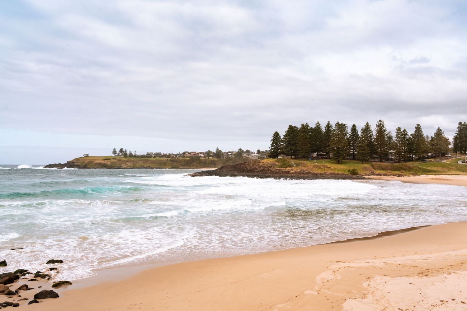 Scenic aerial panorama of sandy Kiama beach with waves crashing along the New South Wales coastline on a cloudy day.