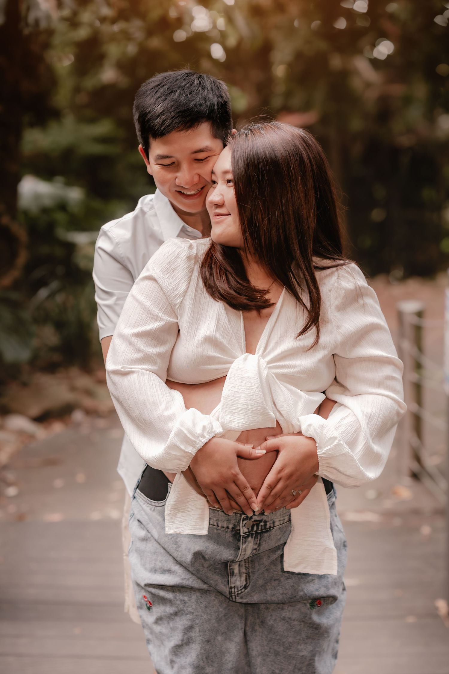 A romantic couple in white shirts embraces outdoors with soft natural lighting and bokeh effect in the background.