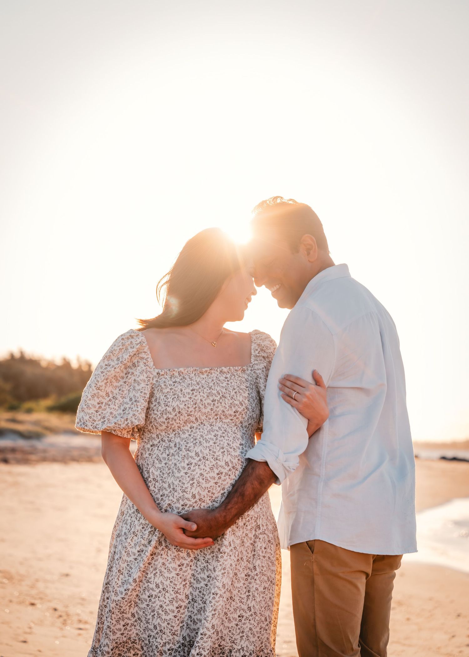 A couple embraces on a beach at sunset, silhouetted against the golden light.