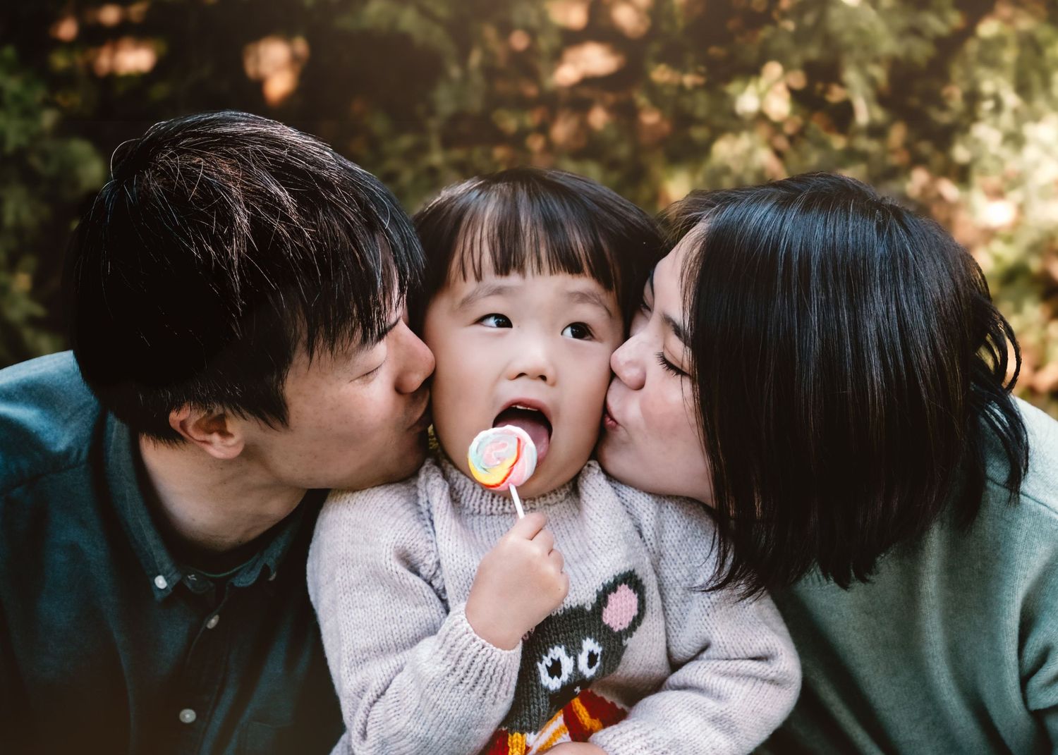 An Asian family shares a sweet moment together while enjoying a lollipop on a sunny autumn day.