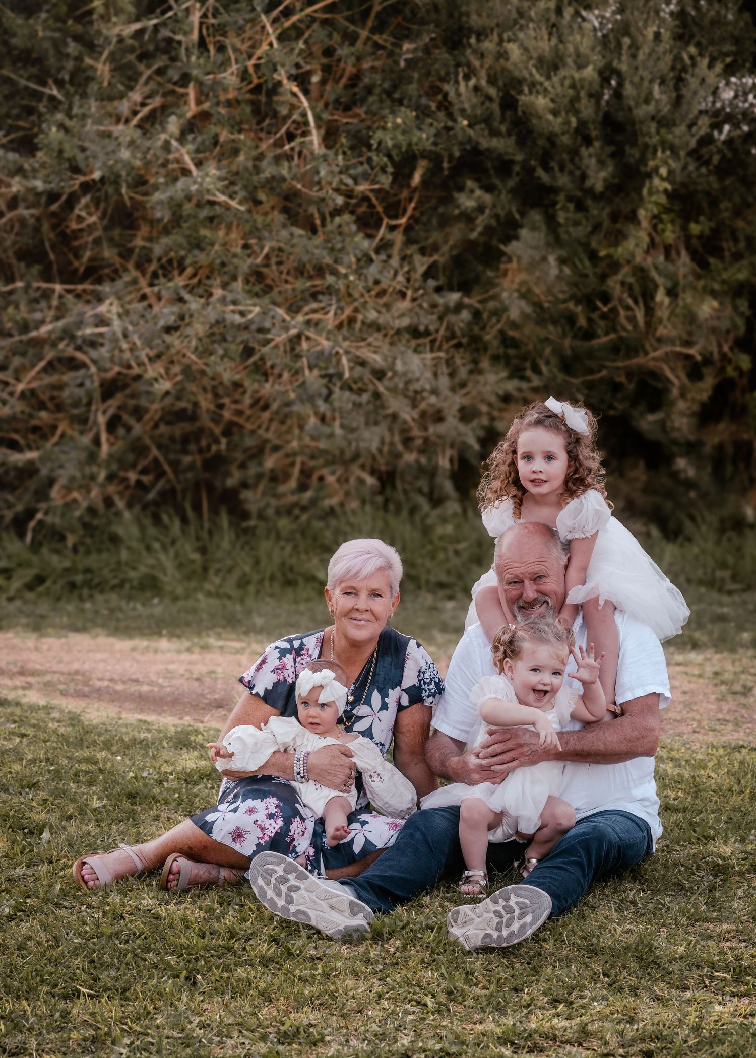 Family members sitting together on grass in casual outdoor photo session with natural lighting and autumn backdrop.