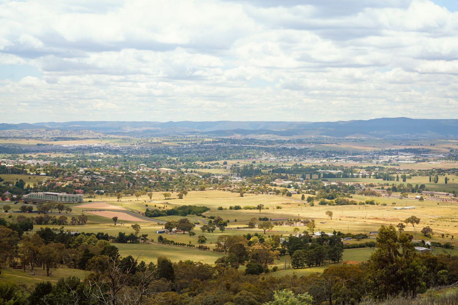Scenic panorama of a vast rural valley with rolling hills and scattered trees under cloudy skies.