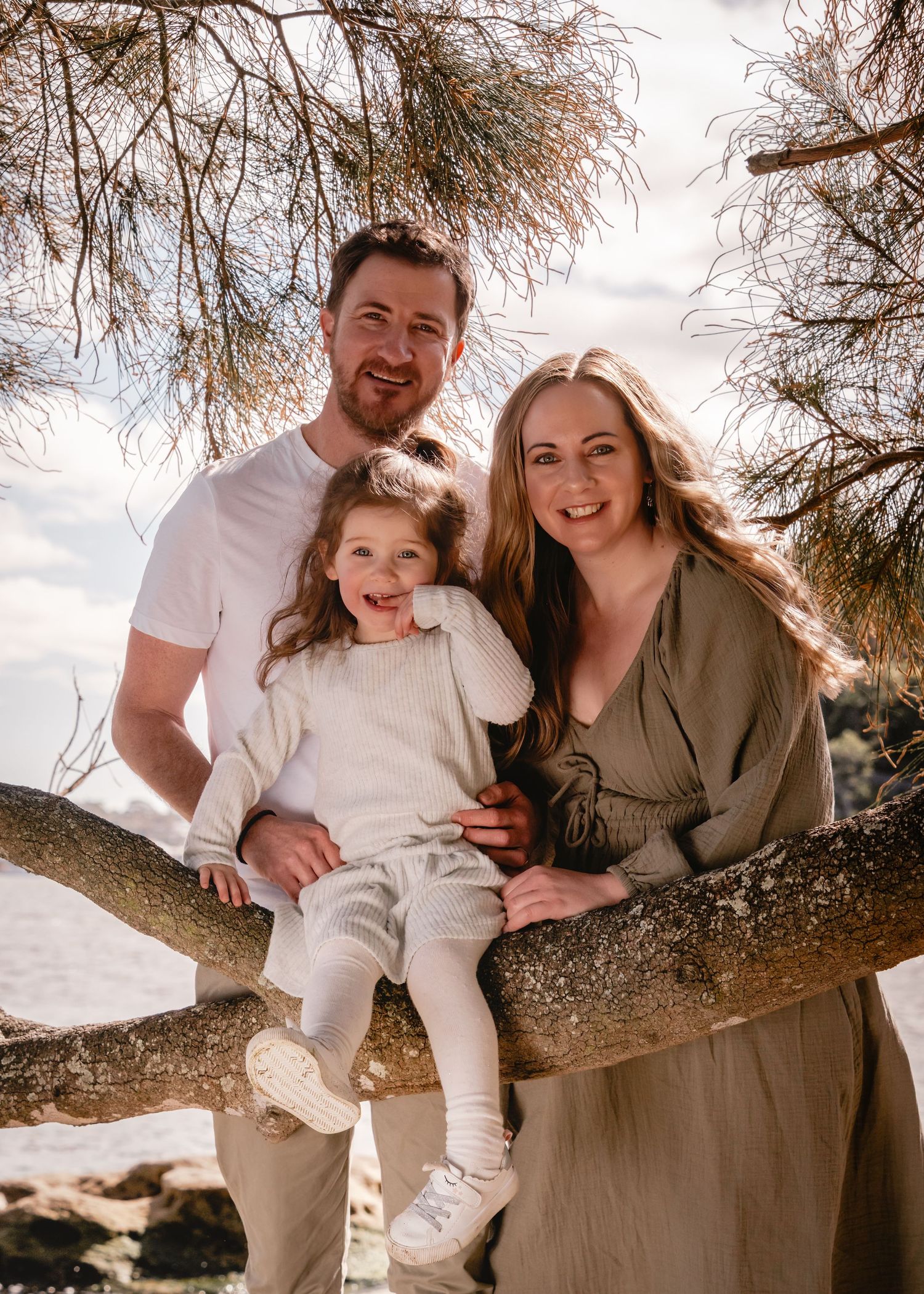 A family sitting and playing together on a large tree branch in an outdoor setting during sunset.