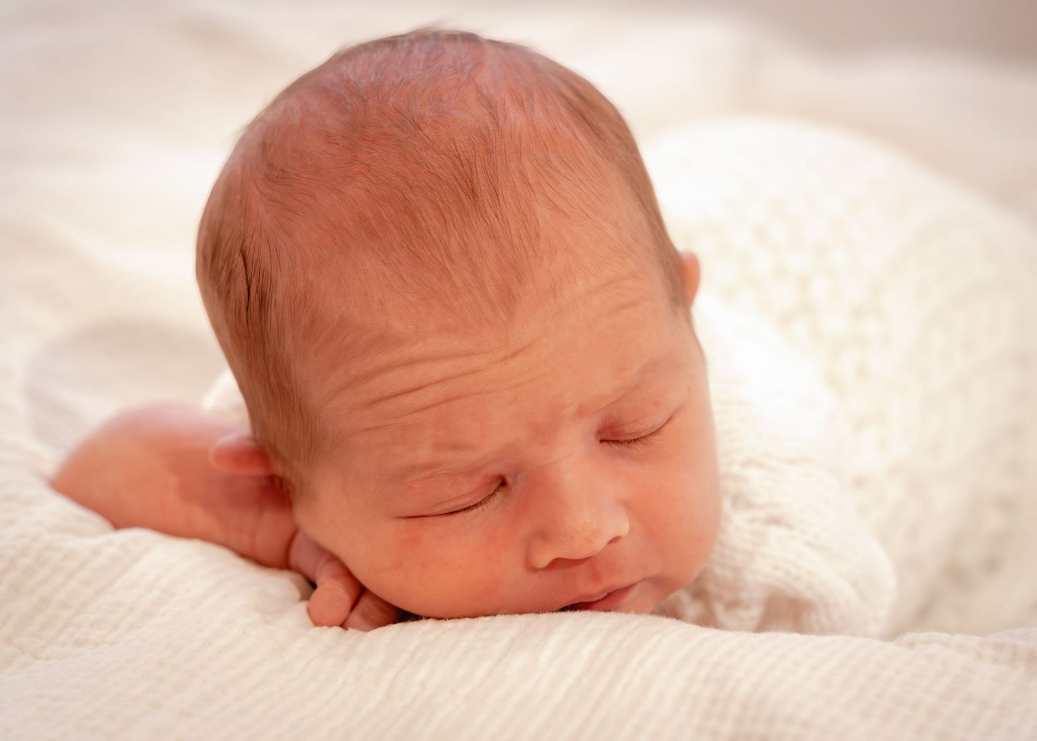A series of gentle close-up shots showing a sleeping newborn baby on soft white bedding.