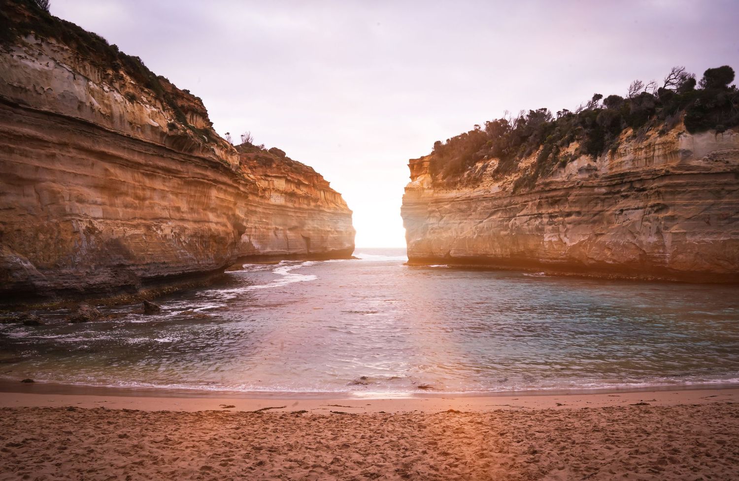 Orange sunlight illuminates limestone cliffs and rock formations along the Great Ocean Road coastline at sunset.