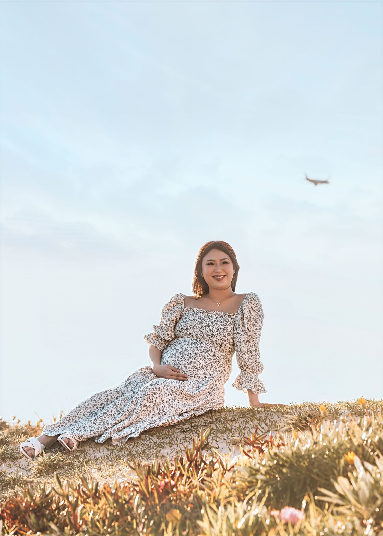 A person in a floral dress relaxes on a grassy hillside during golden hour.