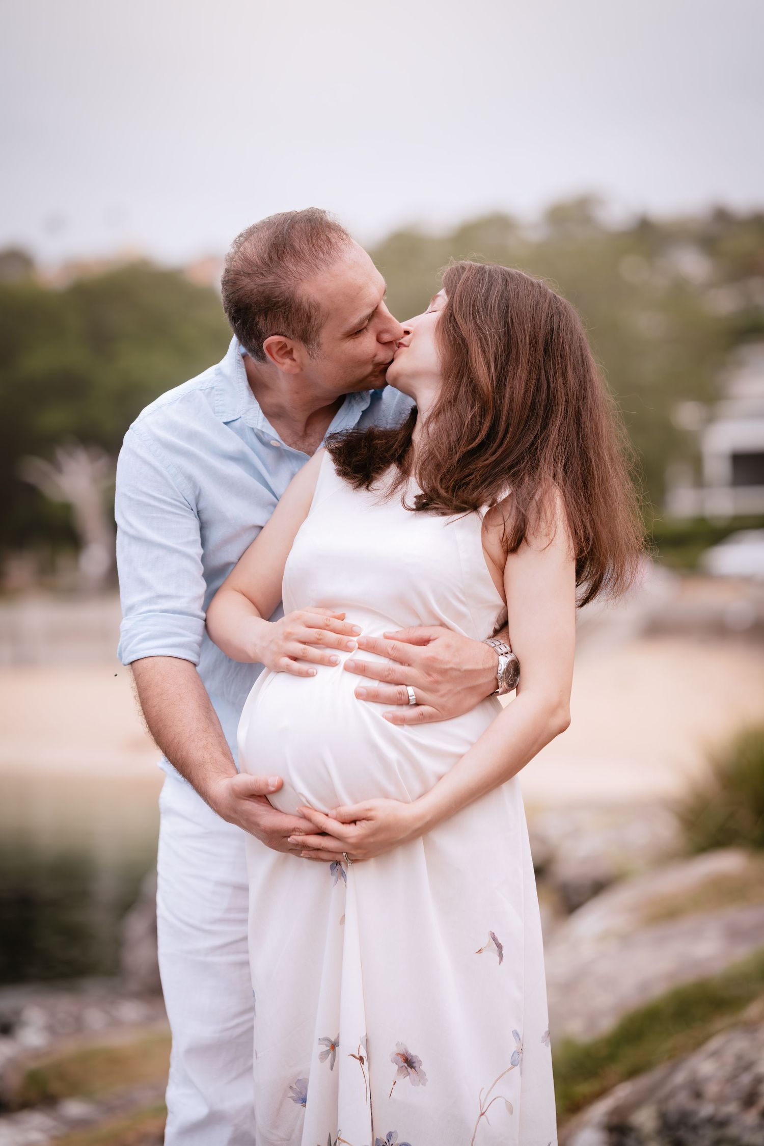 A romantic couple in white outfits embrace and kiss on a beach during a photo session.