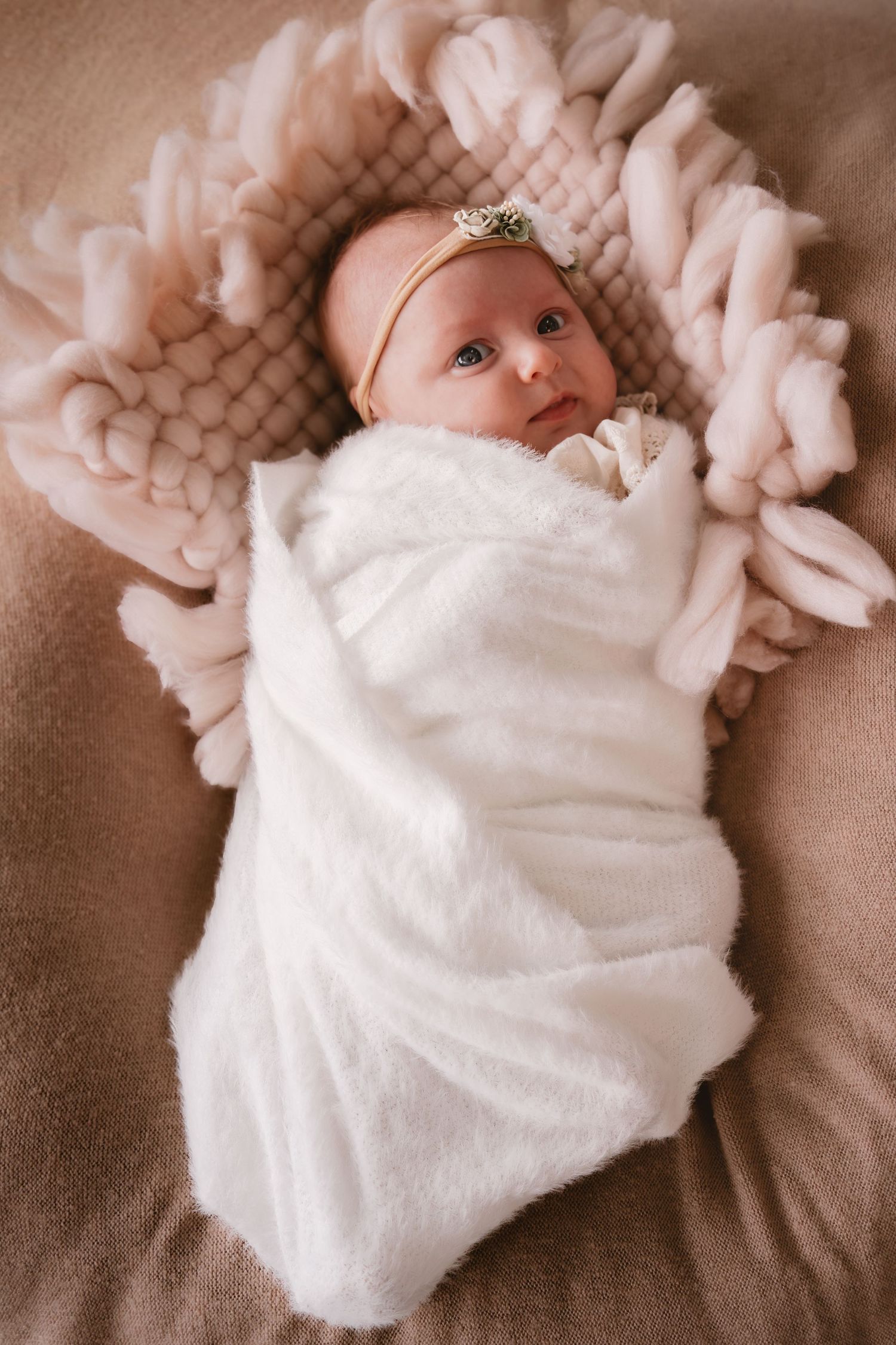 A baby in a soft white blanket lies on a beige surface in a series of connected photos showing different angles.