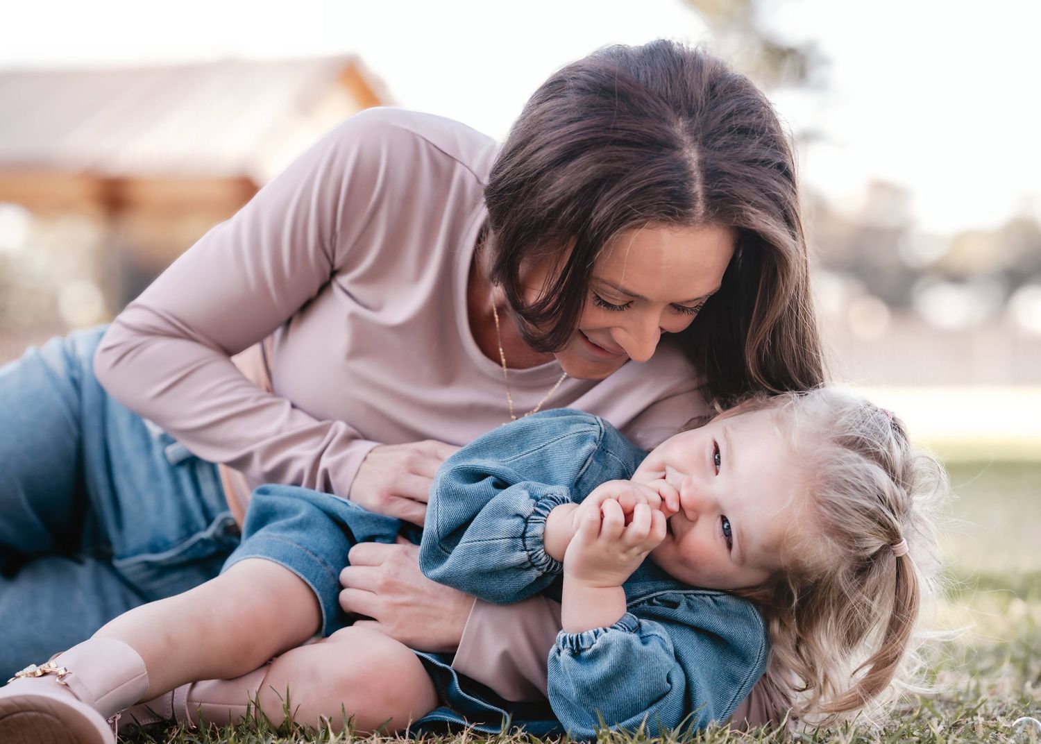 A playful moment shared between parent and child as they laugh together on the grass outdoors.