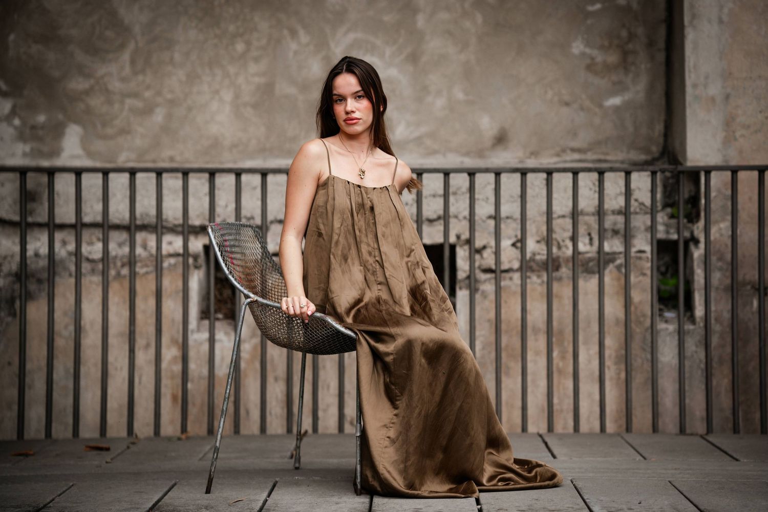 A woman in a brown dress poses gracefully against a stone railing in a series of artistic outdoor portraits.