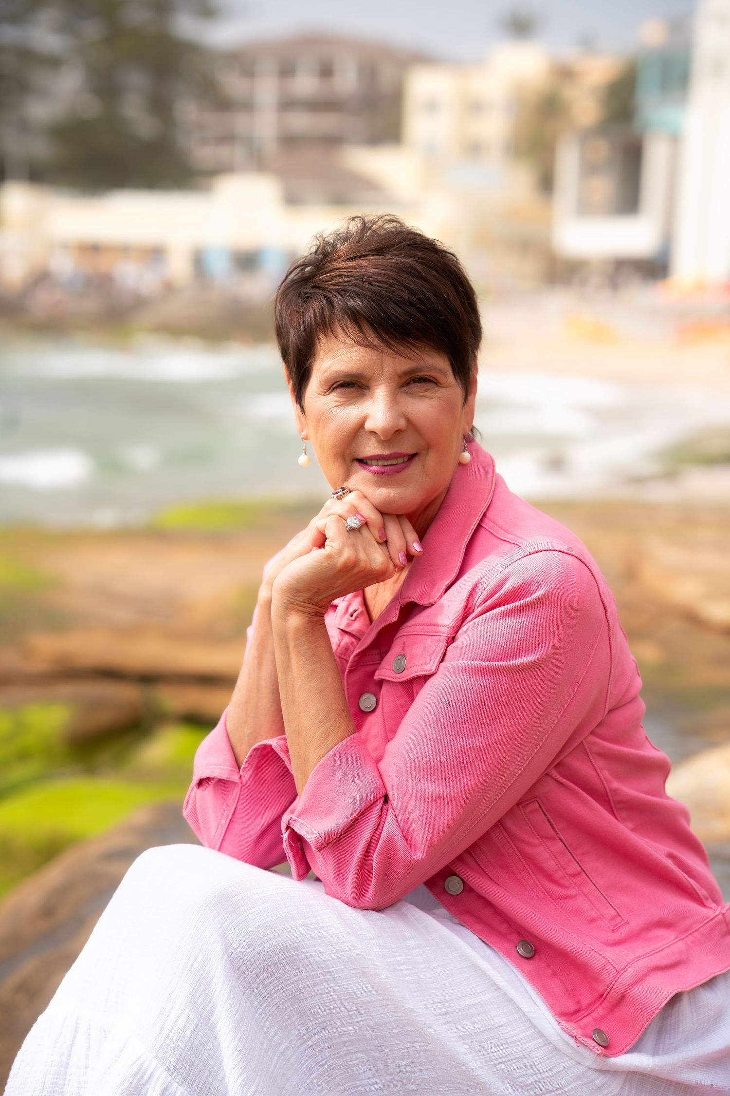 A person in a bright pink blazer sits outdoors while resting their head on their hand.