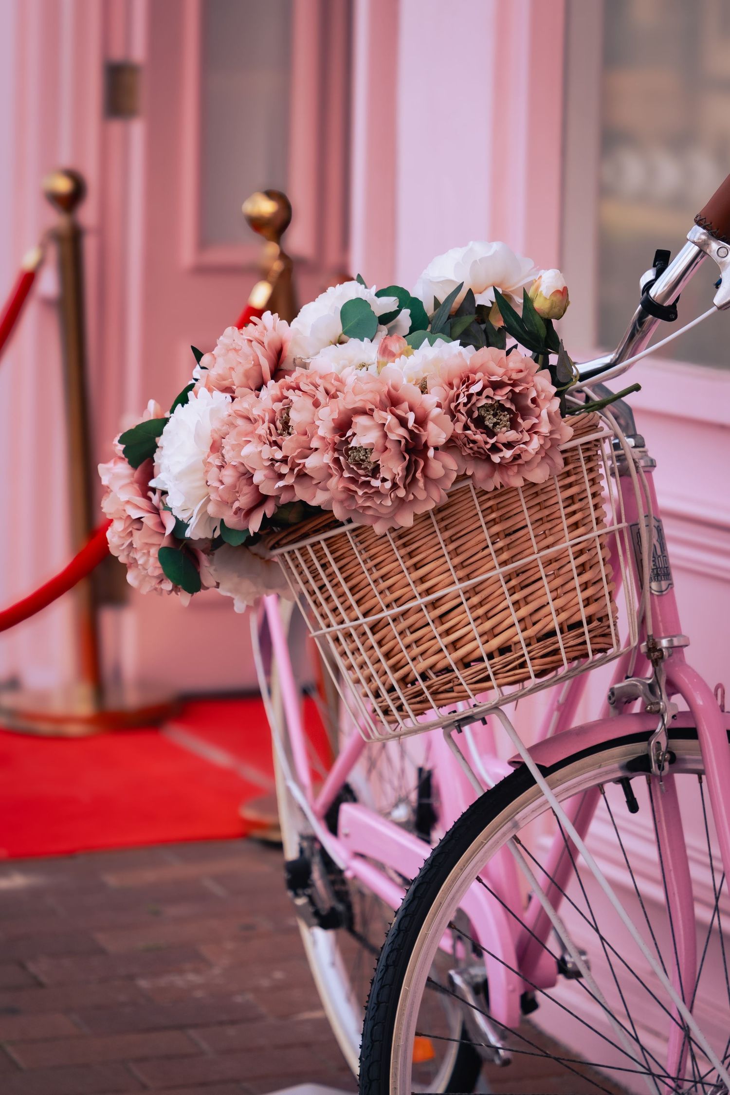 A vintage bicycle with pink flowers in its wicker basket against a rosy pink background creates a romantic scene.