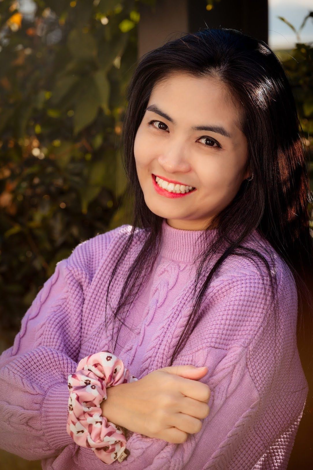 Woman in lavender sweater poses outdoors with warm expressions against a blurred natural background.