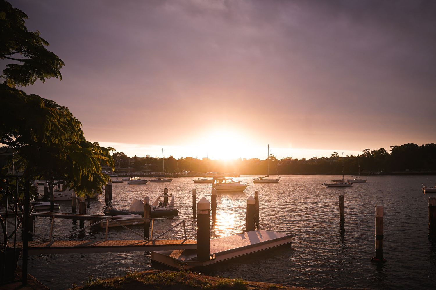 Beautiful sunset over a waterfront dock with boats silhouetted against the golden sky and calm waters.