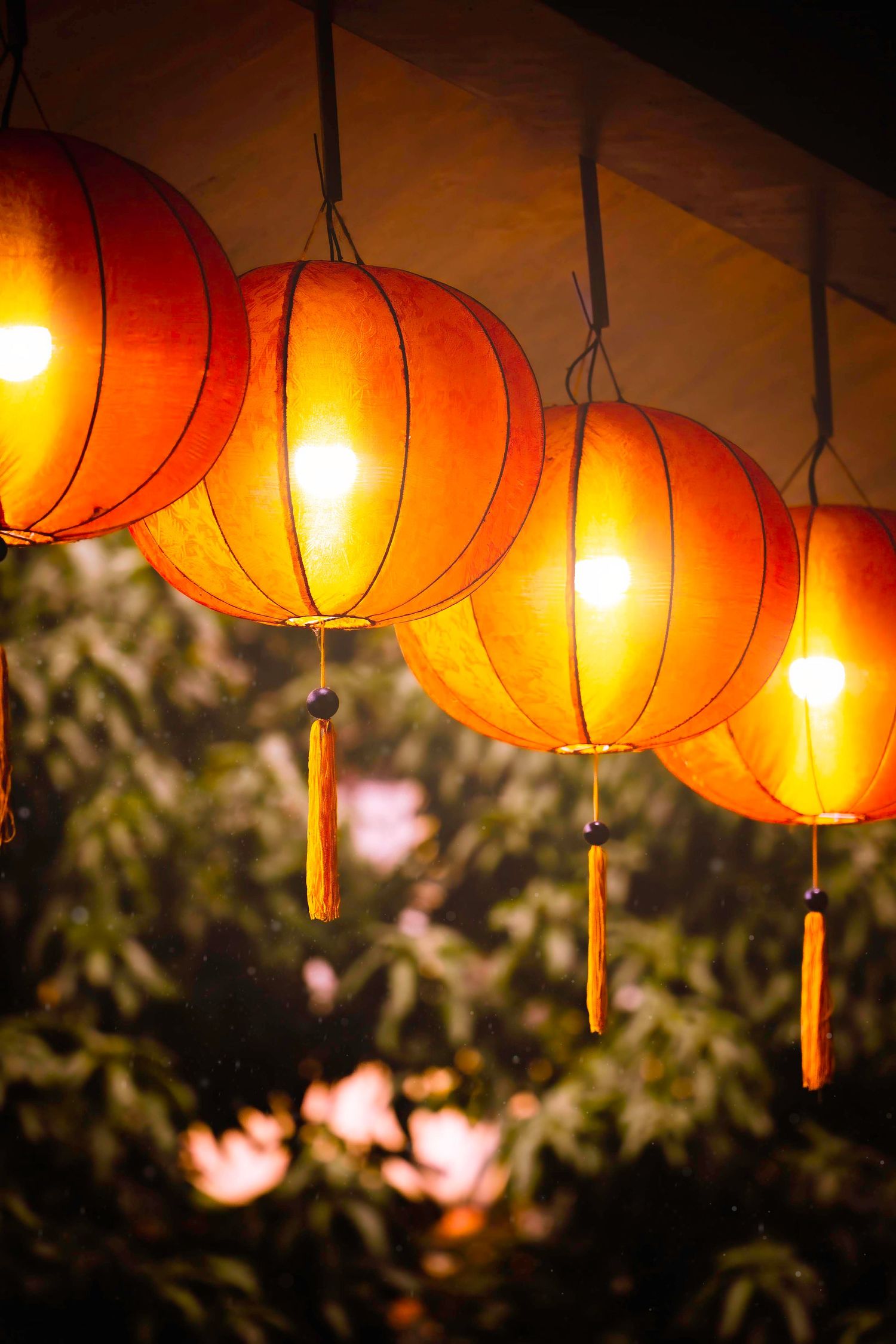 Glowing orange Chinese paper lanterns illuminate the evening sky with a warm ambient light against foliage.