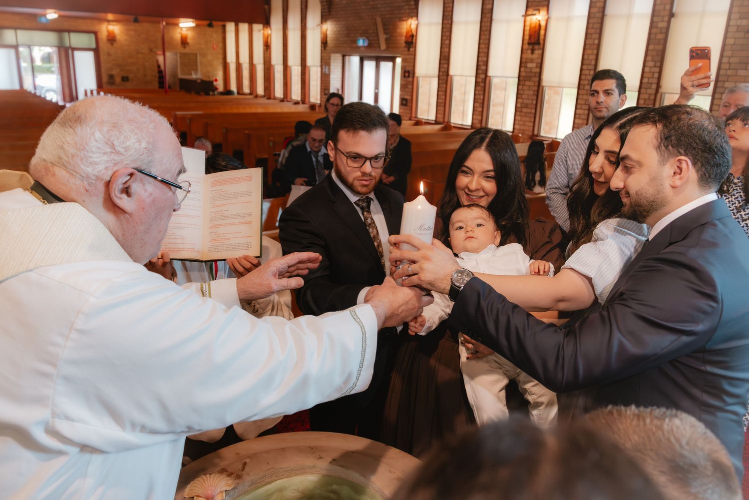 Priest performing a baptism ceremony with family holding a candle in a church.
