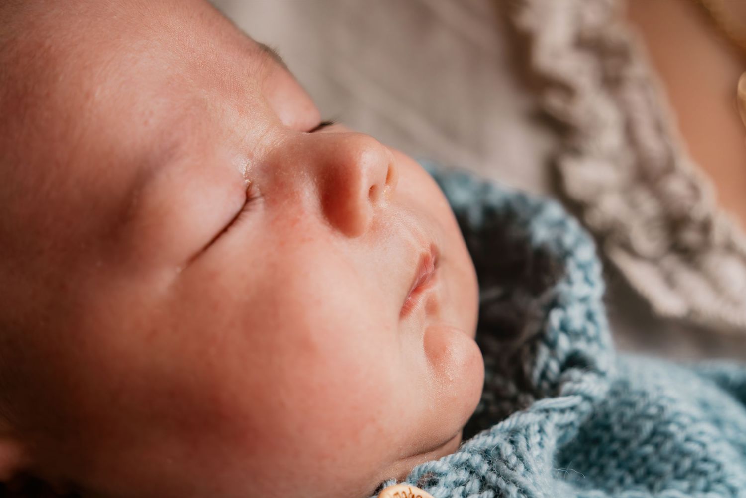 Sleeping newborn baby wrapped in soft blue knit blanket with peaceful expression in natural lighting.