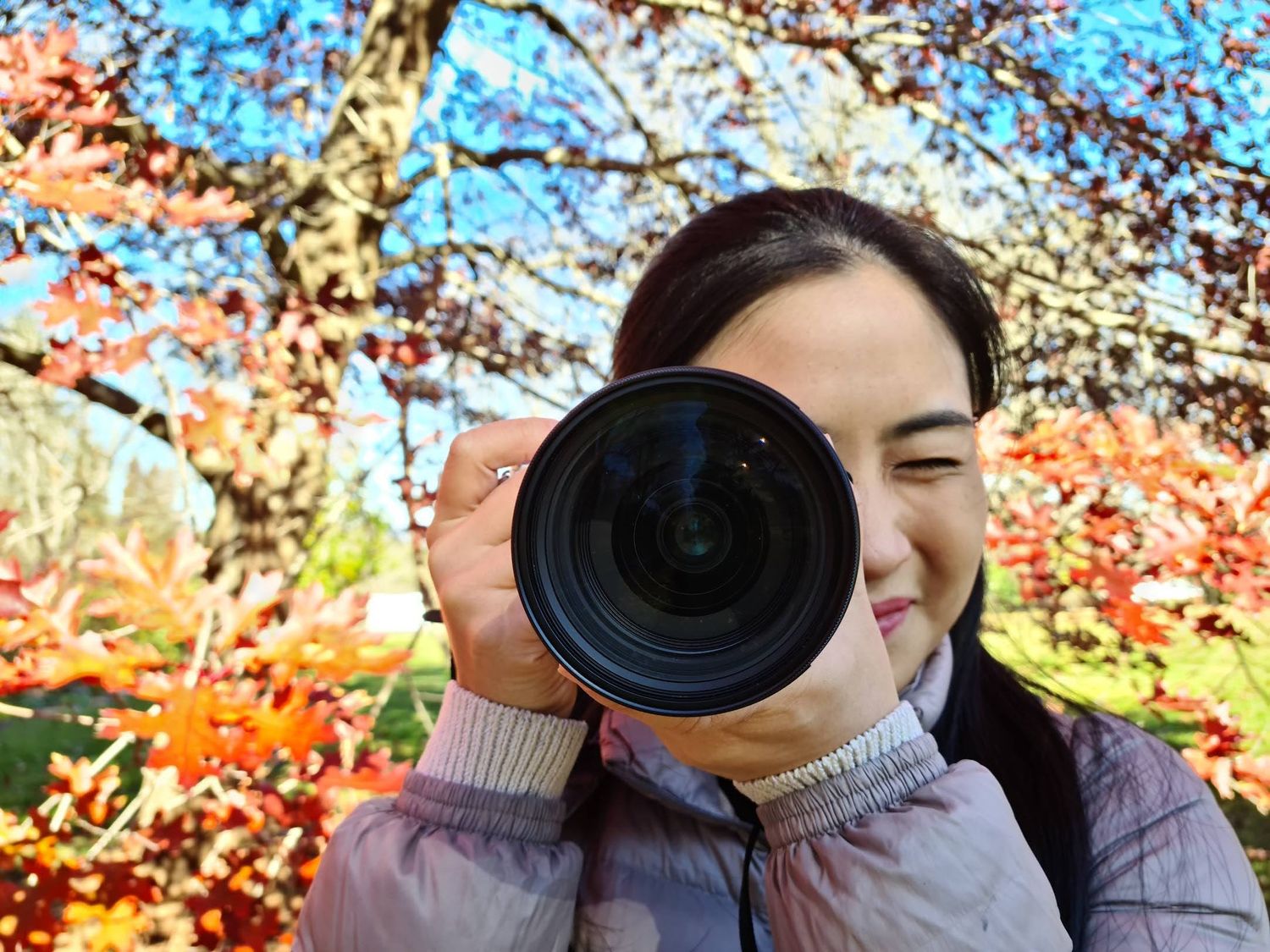 Photographer with professional camera lens against vibrant autumn foliage and blue sky background.