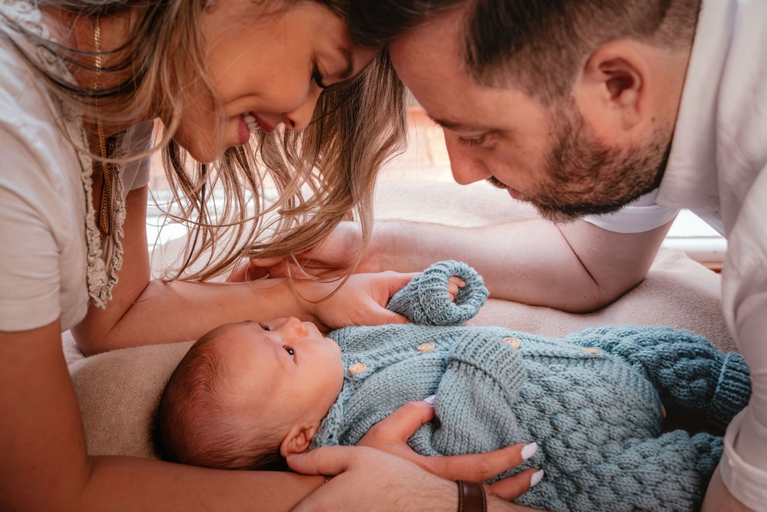 A loving family with a newborn baby sharing tender moments together in a cozy white bedroom setting.