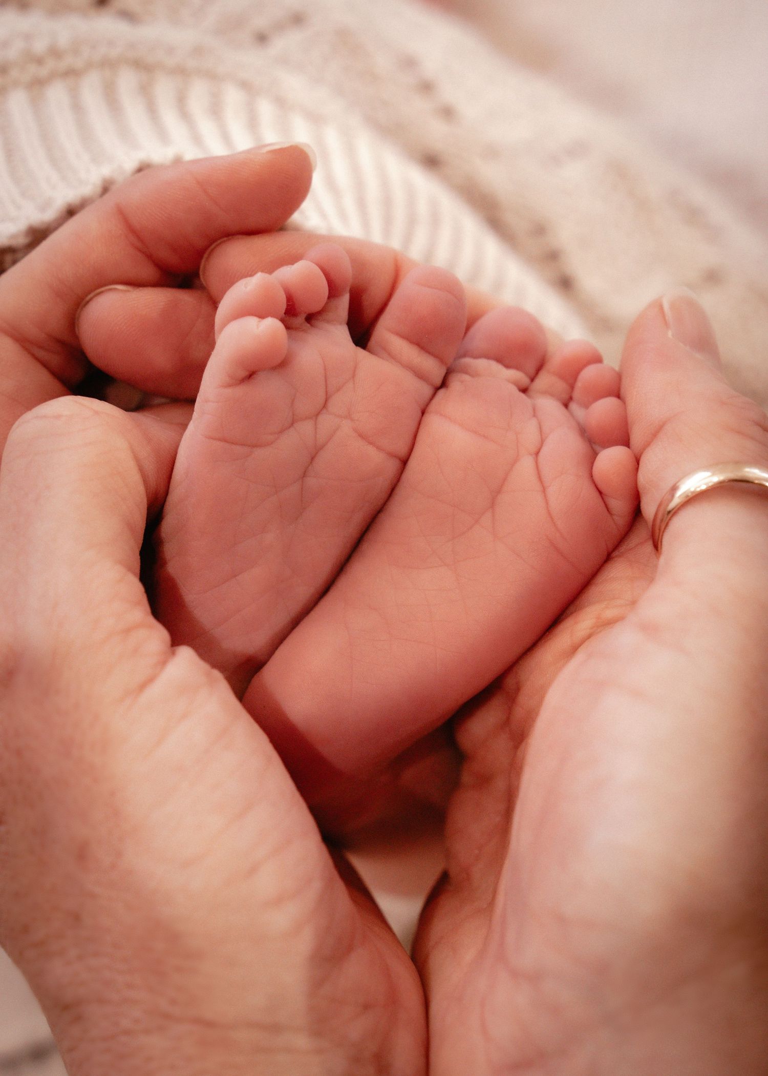 Tiny newborn baby feet cradled gently in adult hands against a soft white knitted blanket background.