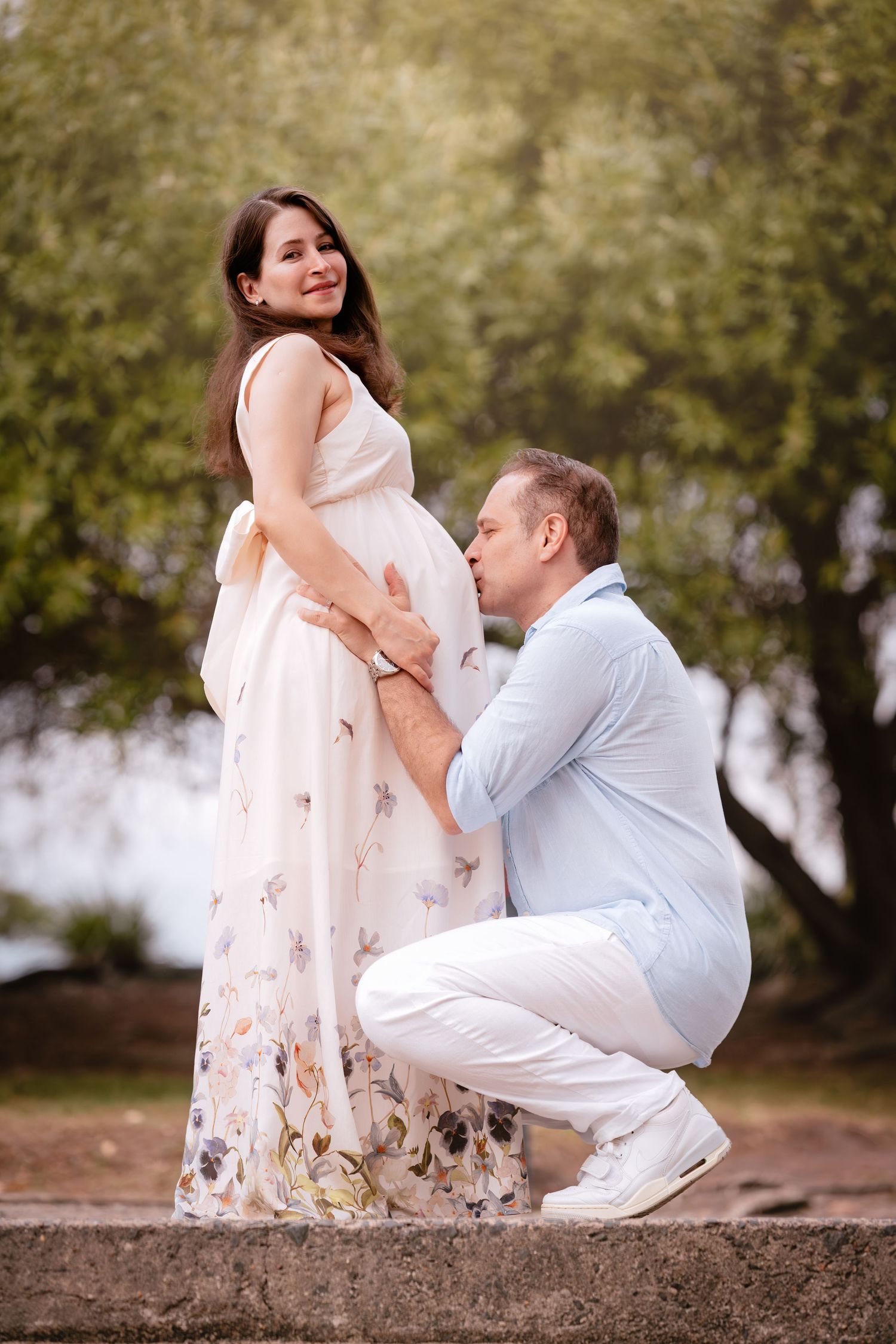 A romantic outdoor maternity photoshoot sequence showing a couple in white outfits sitting on a rustic log.