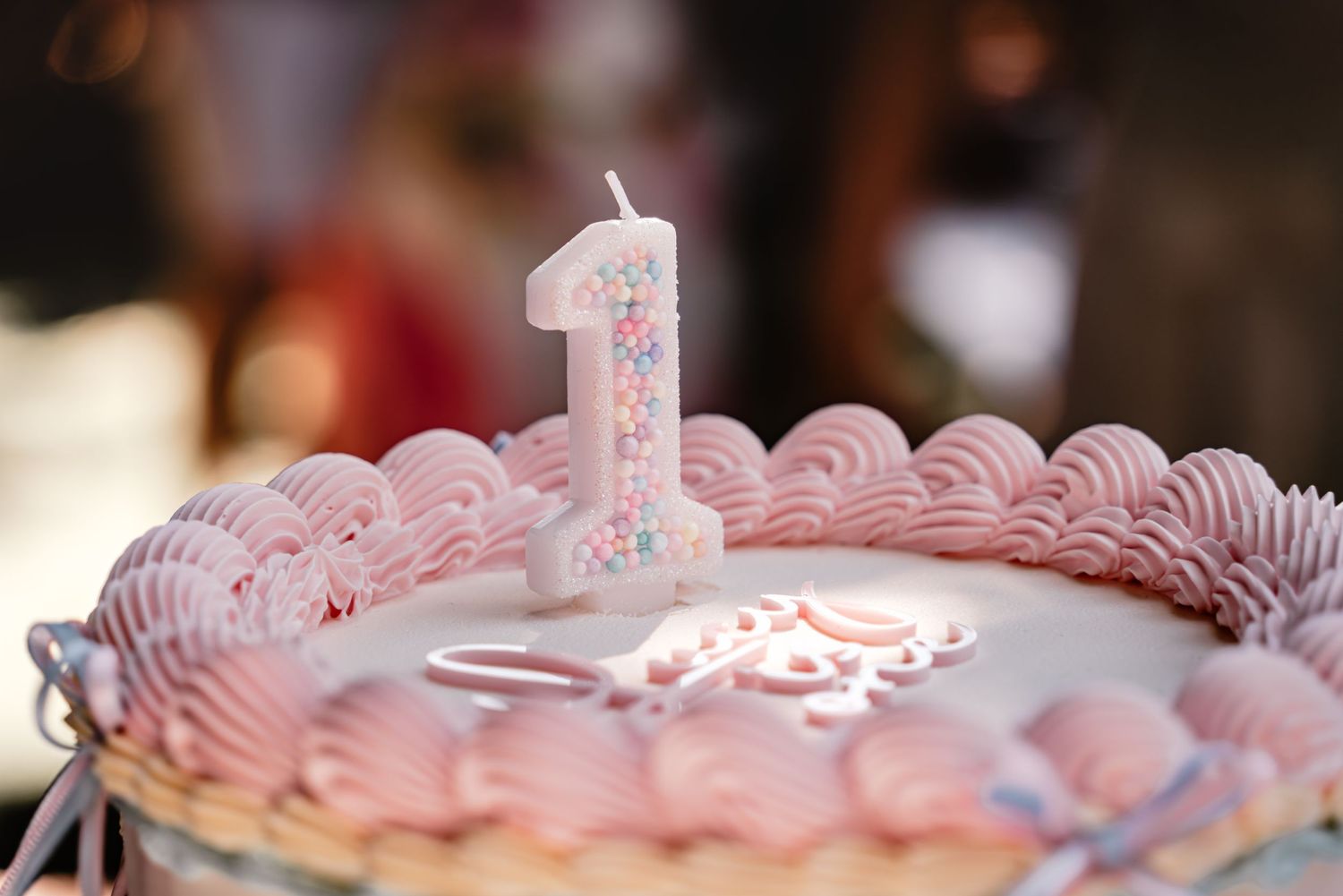 A pink and white first birthday cake decorated with rosette frosting and a number one candle on top.