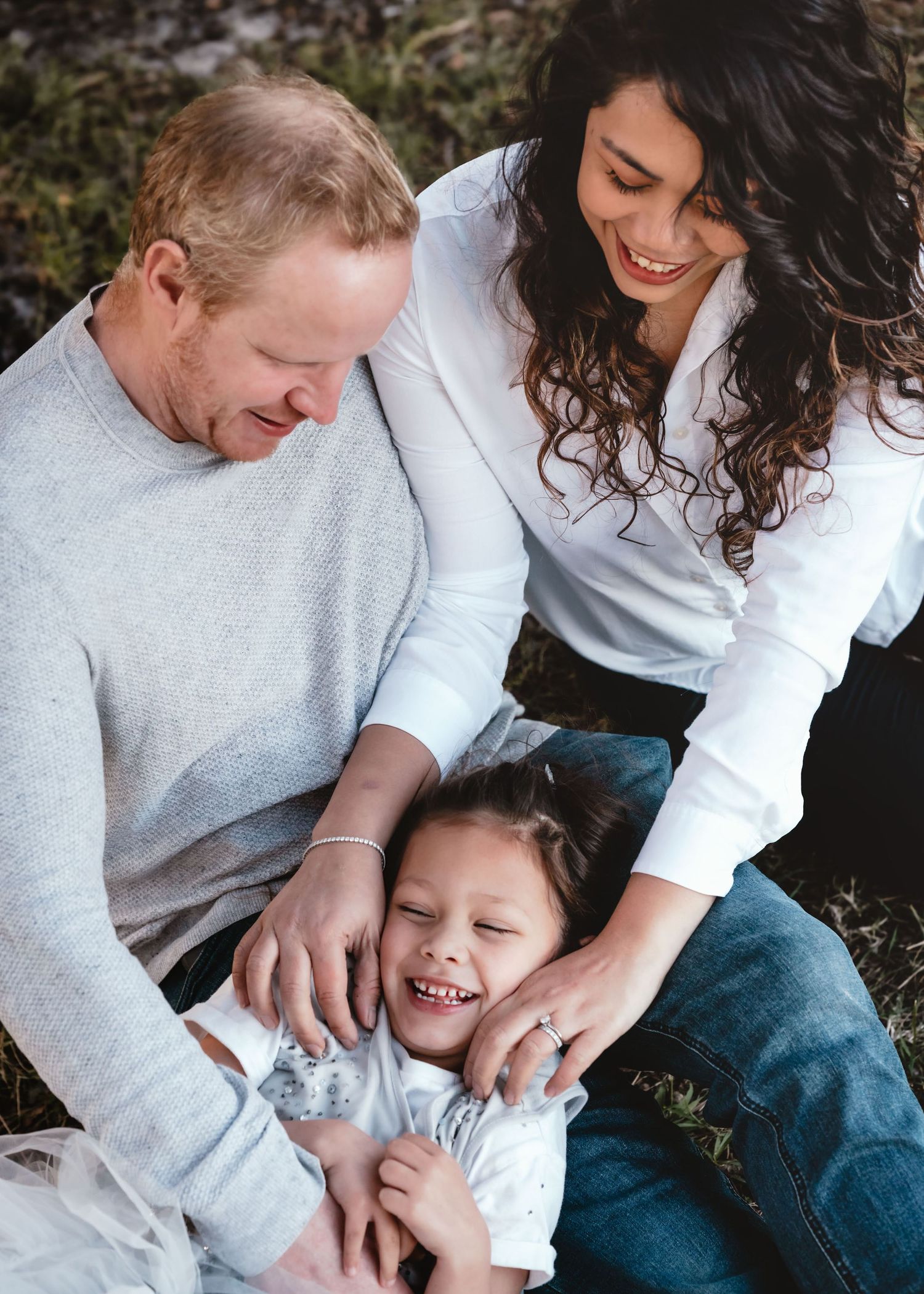 A family shares a joyful moment together while tickling and laughing outdoors in casual attire.