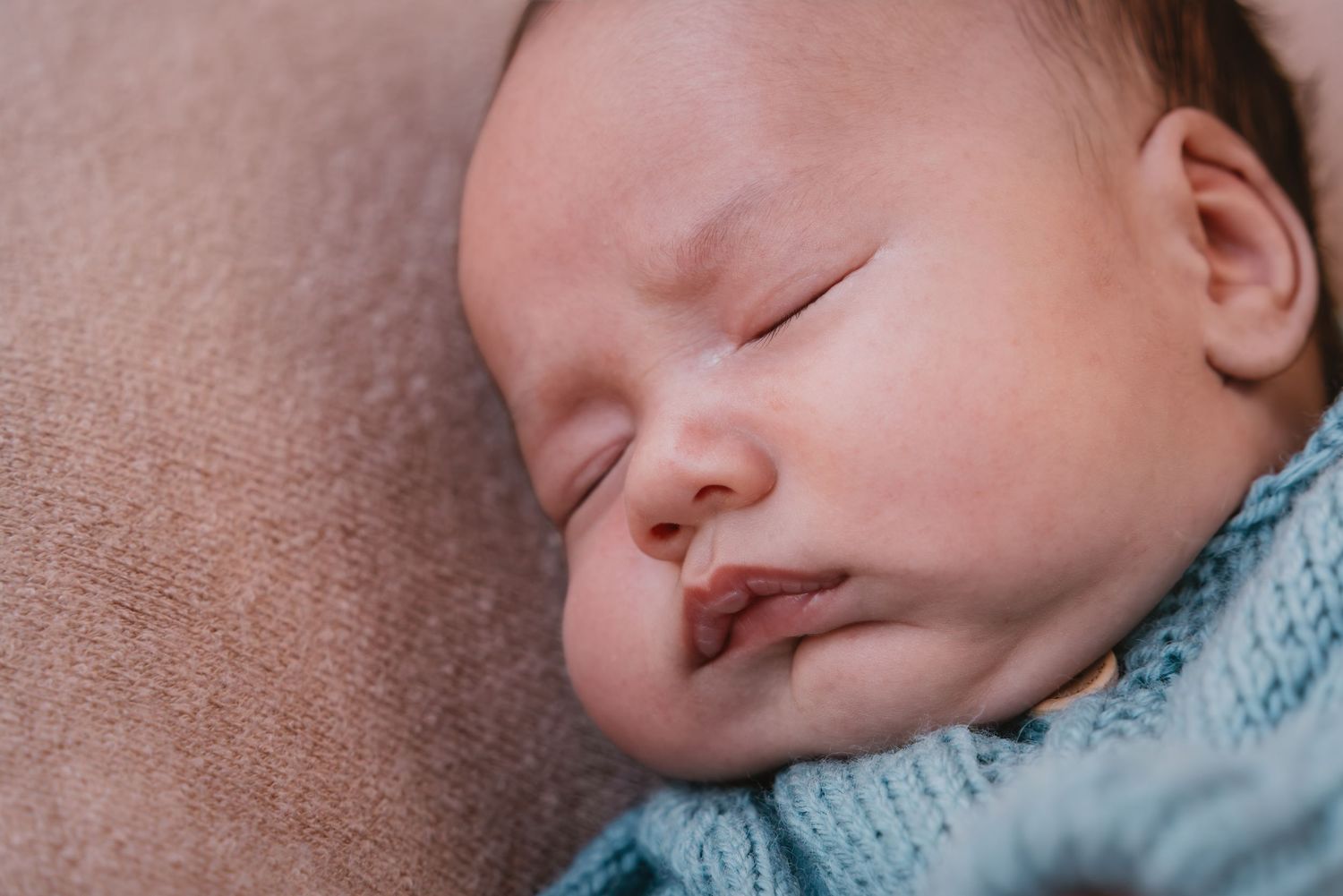 Peaceful sleeping baby wrapped in soft blue knitted blanket resting on grey surface.