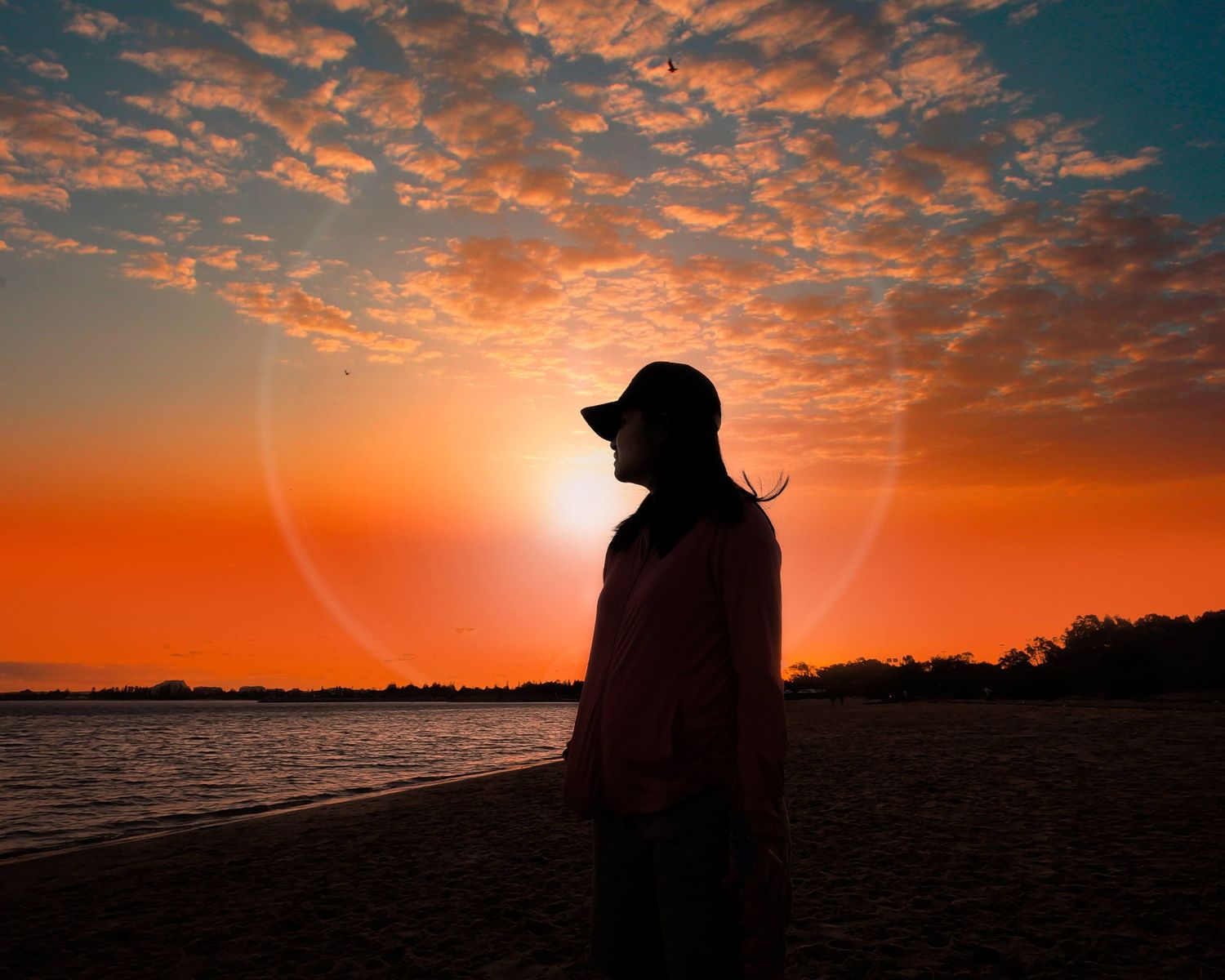 Silhouette of a photographer capturing a vibrant orange and blue sunset over a tranquil lake.