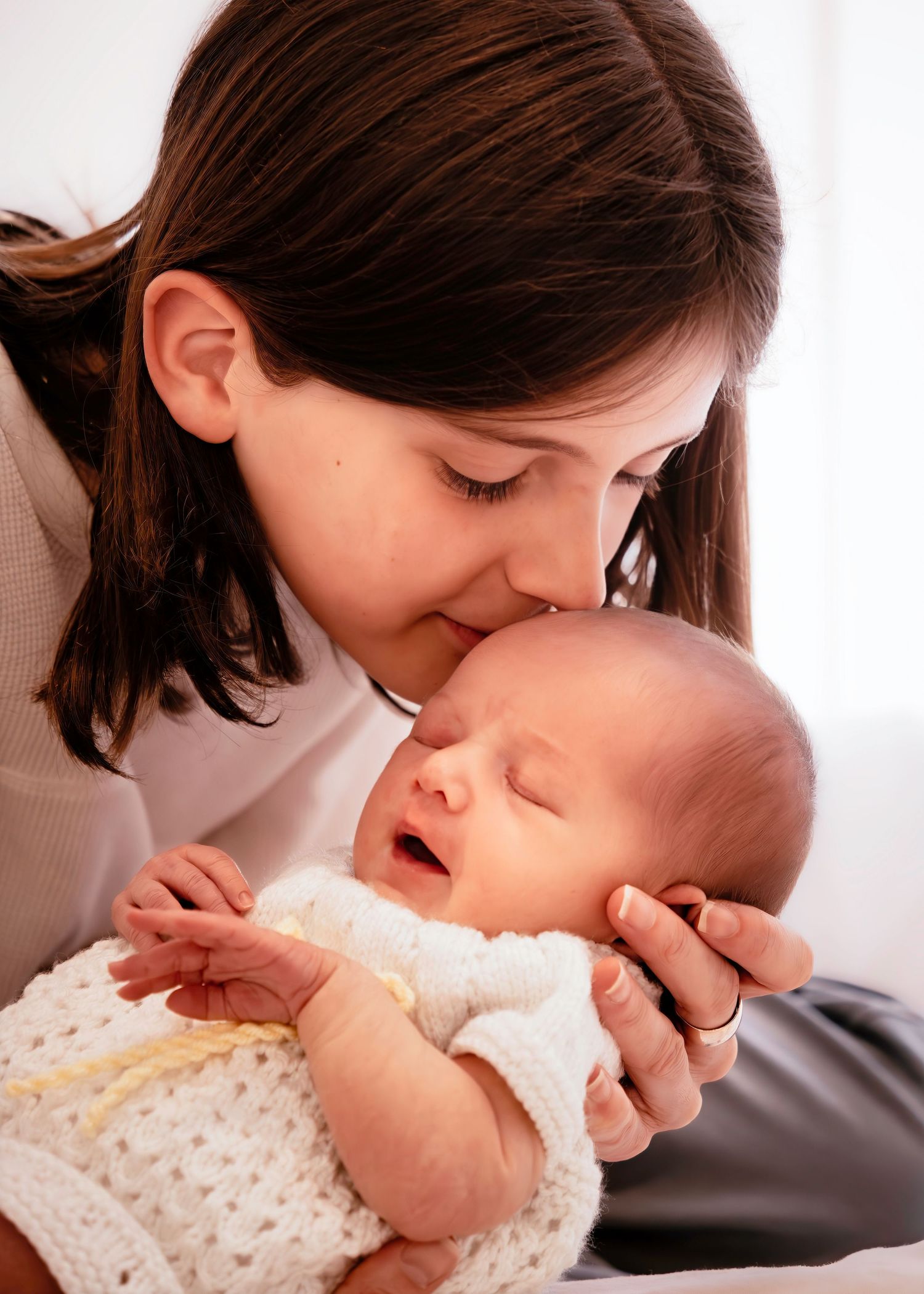 A tender moment shows someone kissing a baby's tiny hand while both wear soft white clothing.
