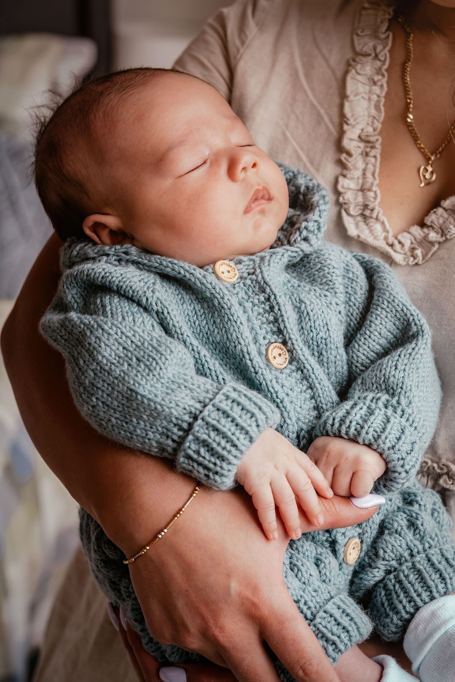 Sleeping newborn baby wearing a cozy light blue knitted cardigan sweater nestled in gentle arms.