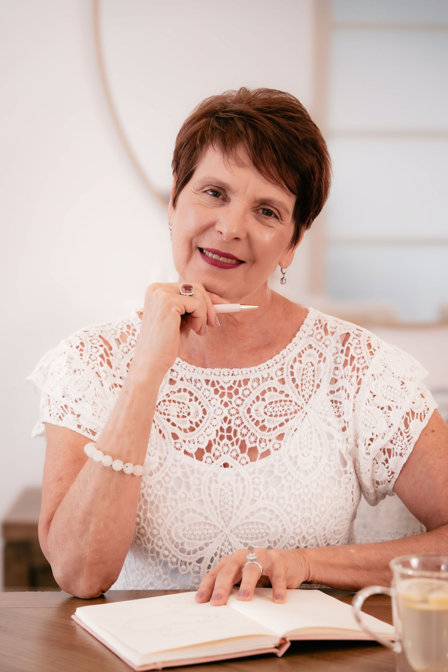 A person in a white lace dress smiles warmly while reading a book with a cup of coffee nearby.