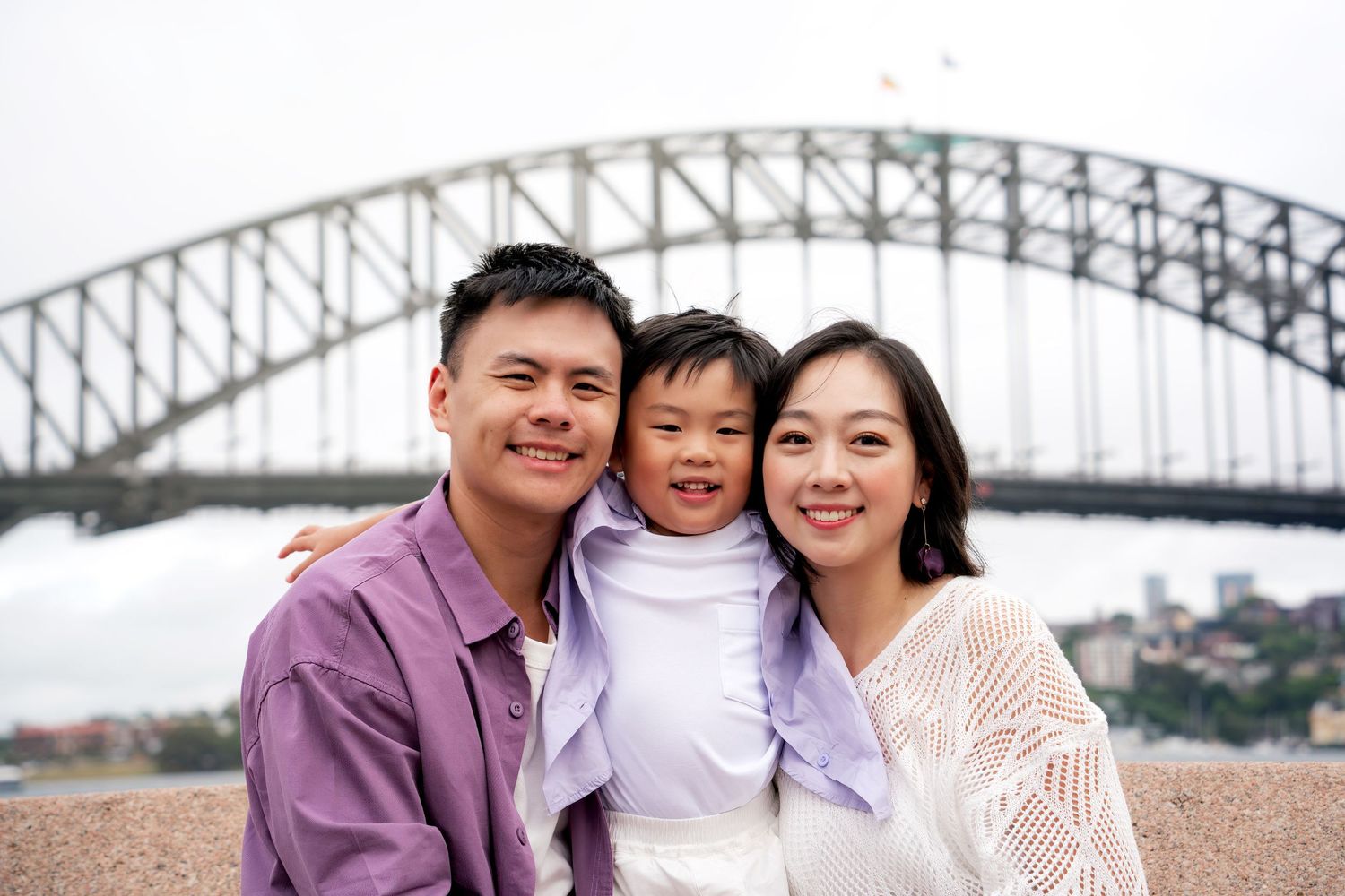 A happy family poses together at multiple locations near the Sydney Harbour Bridge in Australia.