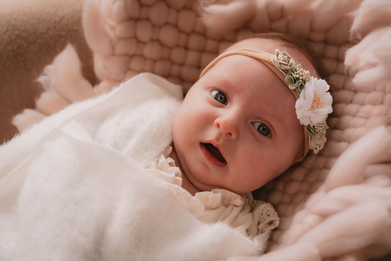 A newborn baby wearing a white headband rests on soft pink fabric in a series of sweet portraits.