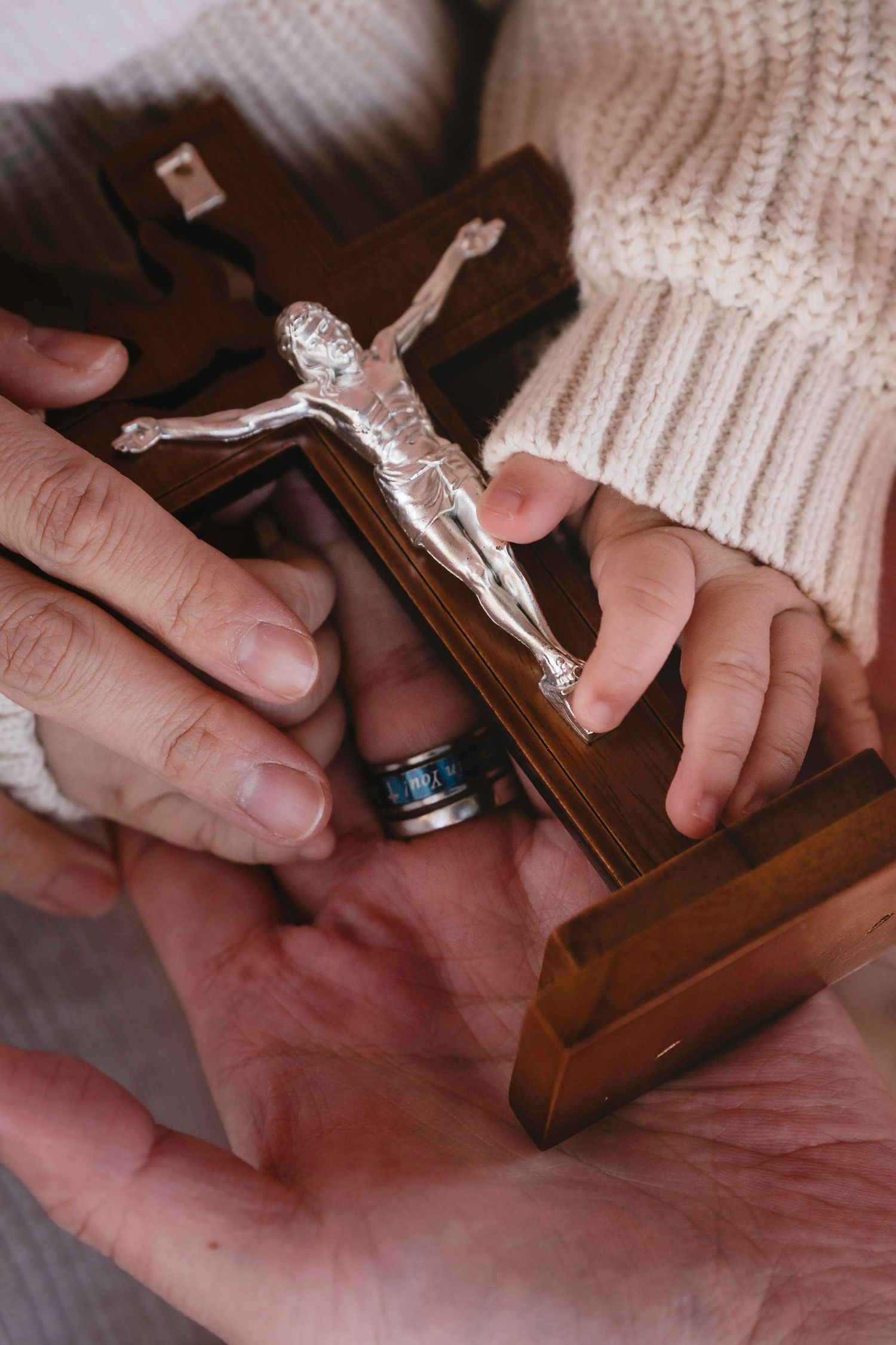 Hands holding a wooden crucifix being tightly grasped in a sequence of close-up images against a white knit background.