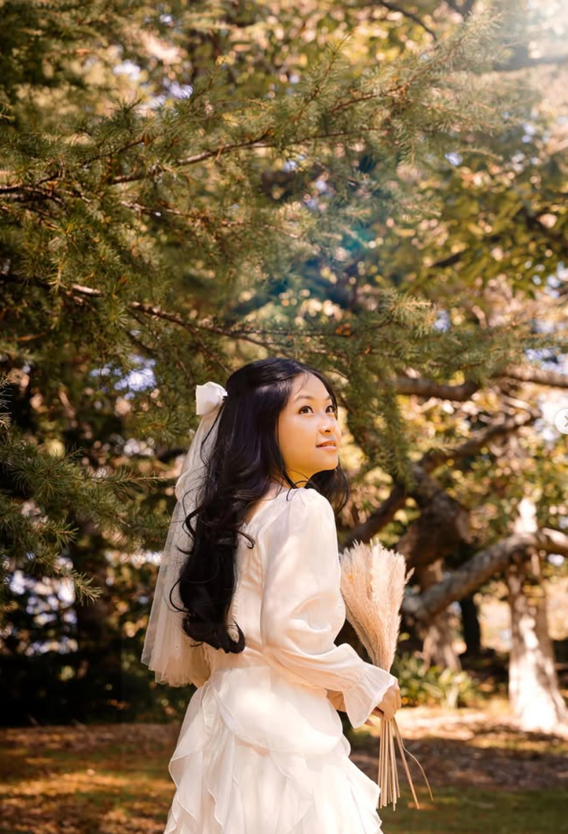 A bride in white poses gracefully among autumn trees during a dreamy outdoor photo session in a natural setting.
