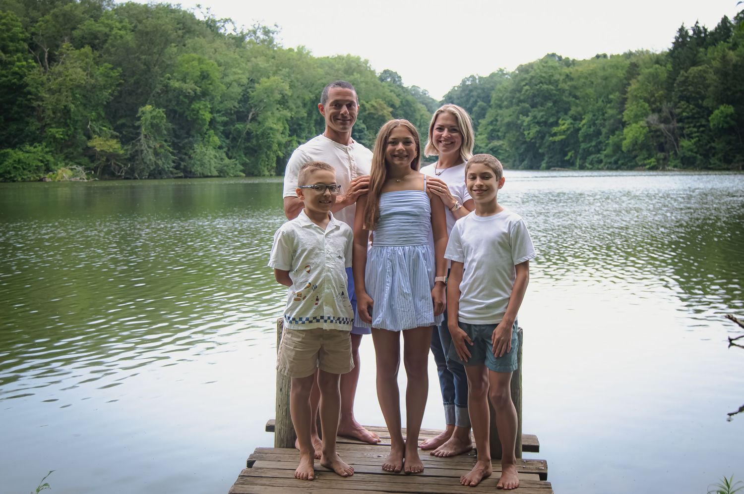 Group portrait at the edge of a tranquil lake surrounded by lush summer trees.