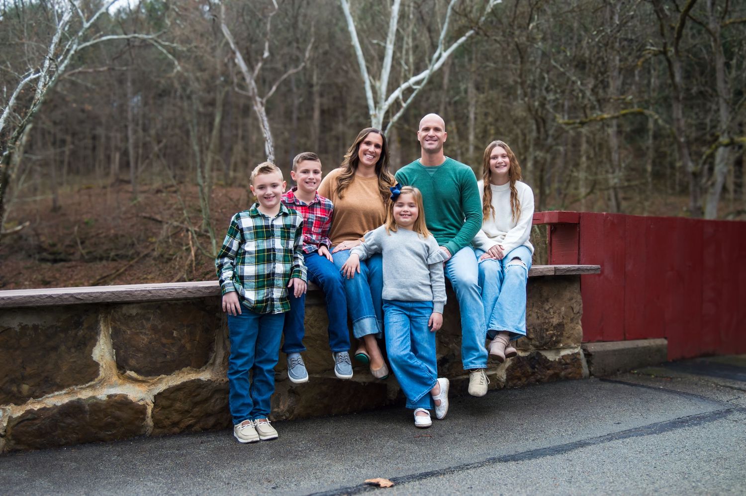 A group sits casually on a wooden bridge railing in coordinating blue and plaid outfits during an outdoor photo session.