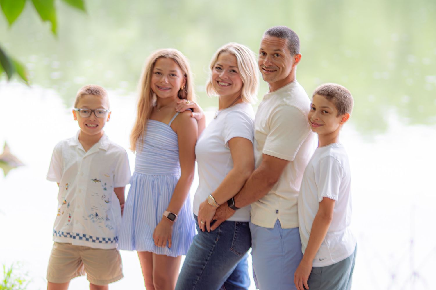 A group poses together outdoors in coordinated light blue and white outfits against a soft blurred natural background.