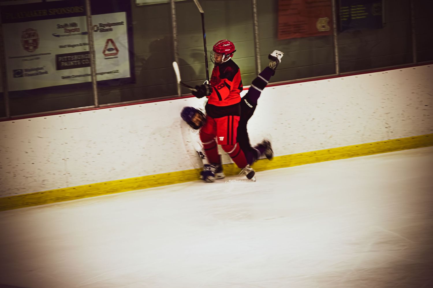 Hockey players in red jerseys practicing along the boards during training session.