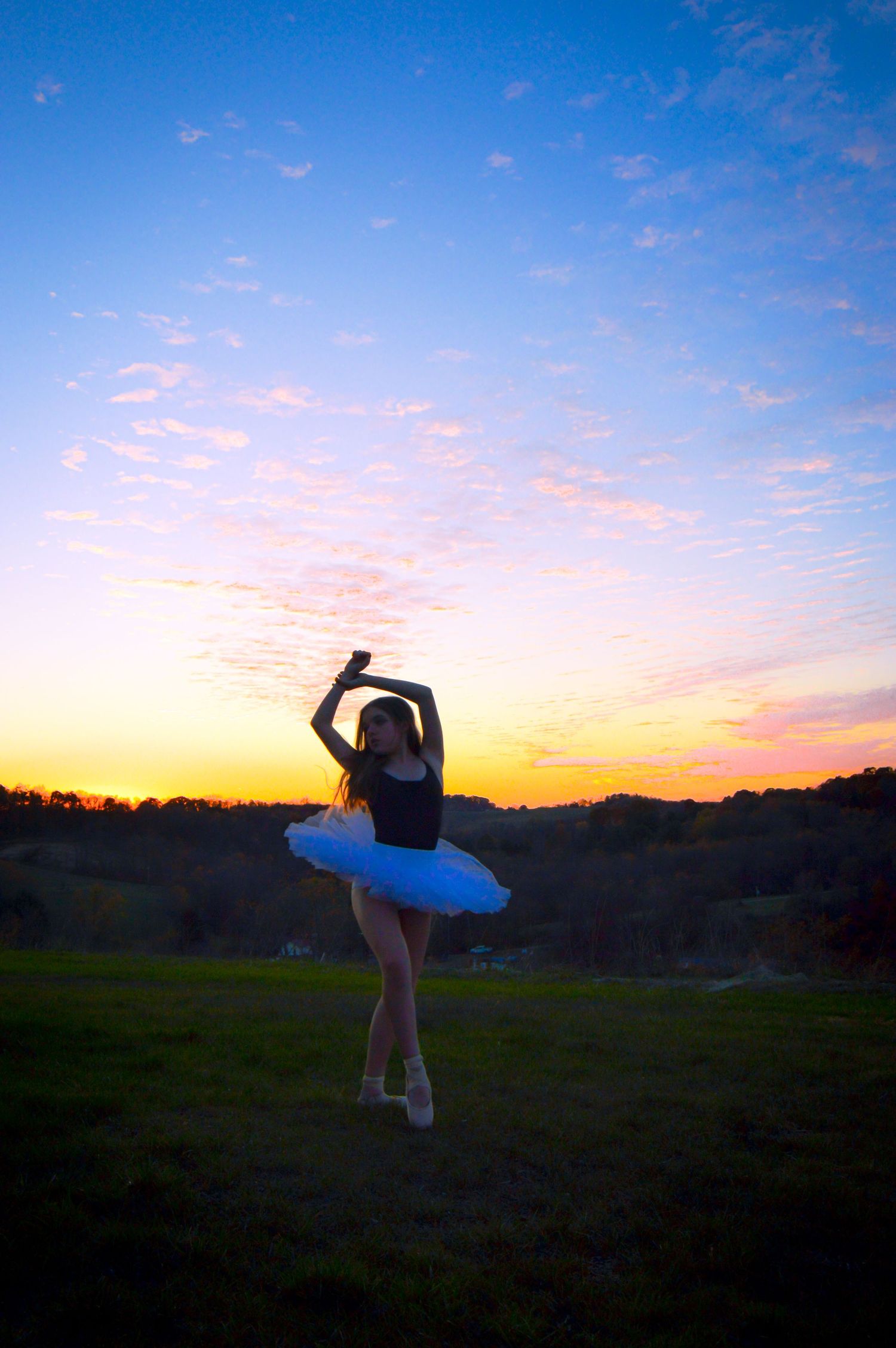 A silhouetted figure strikes graceful dance poses against a vibrant sunset sky over rolling hills.