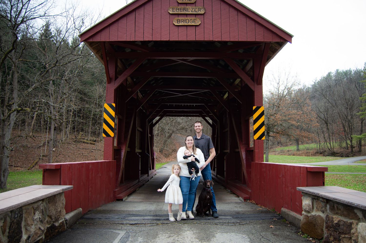 A red covered bridge in rural Pennsylvania with people walking through it on a cloudy autumn day.