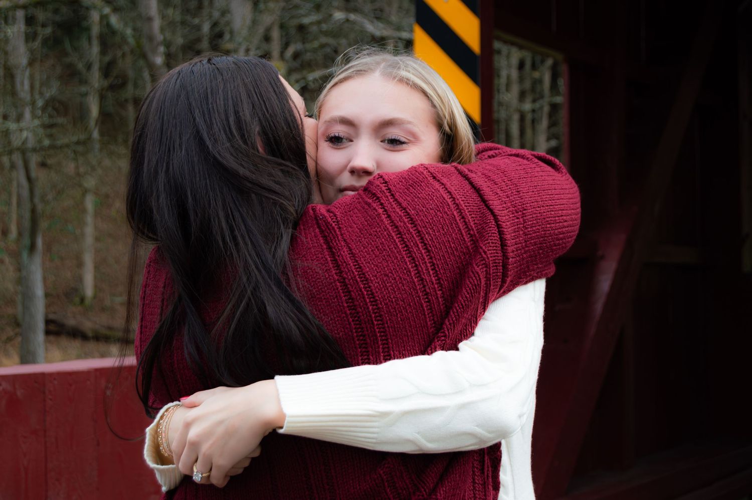 Two people embrace in a warm hug outdoors while wearing winter clothing.