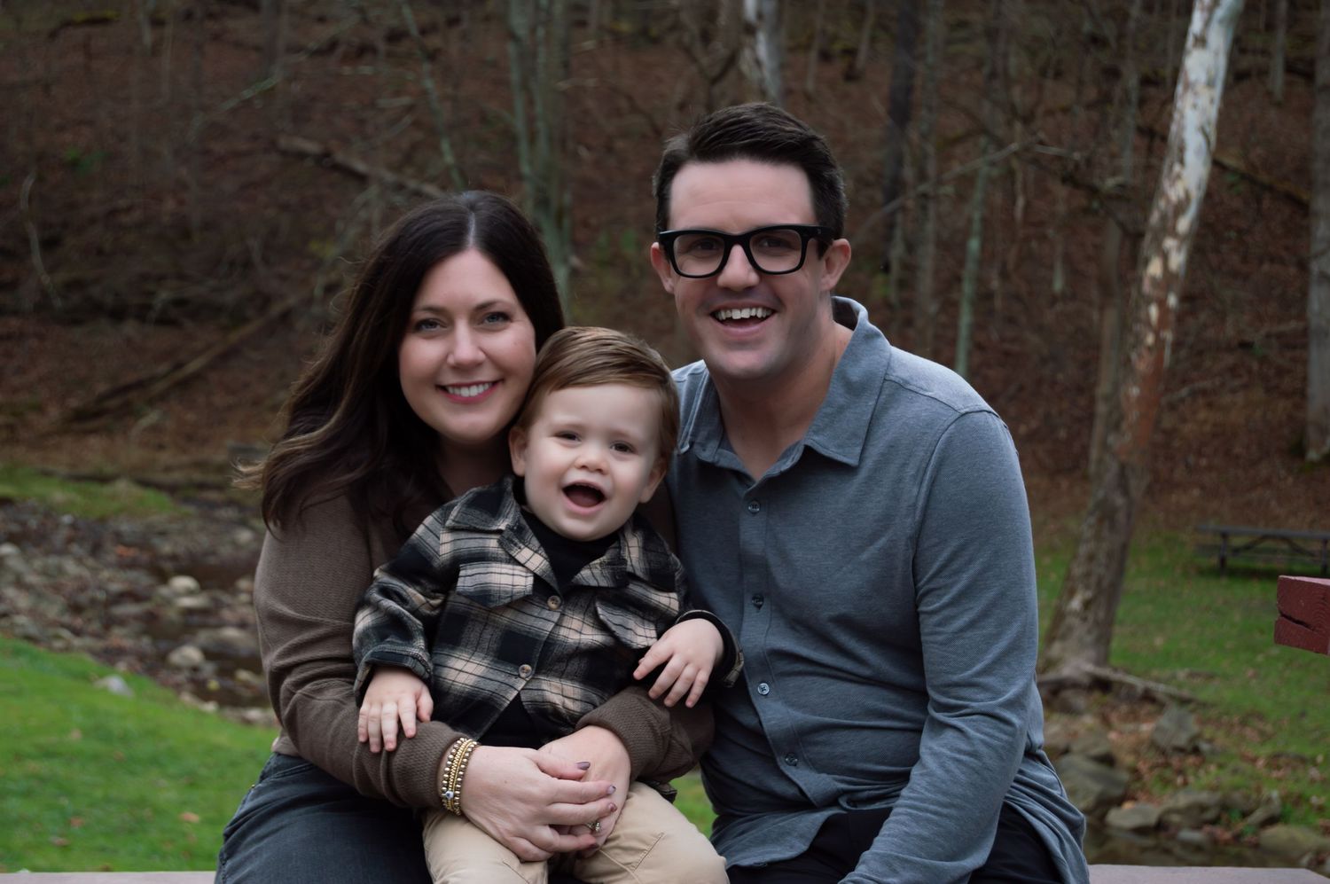 A series of family portraits taken outdoors in a wooded setting showing loving embraces and smiles.
