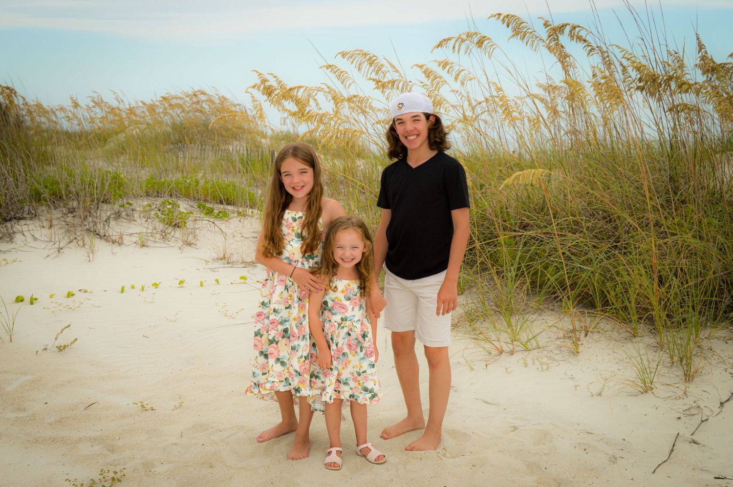 A family poses together on a sandy beach with sea oats swaying in the breeze at sunset.