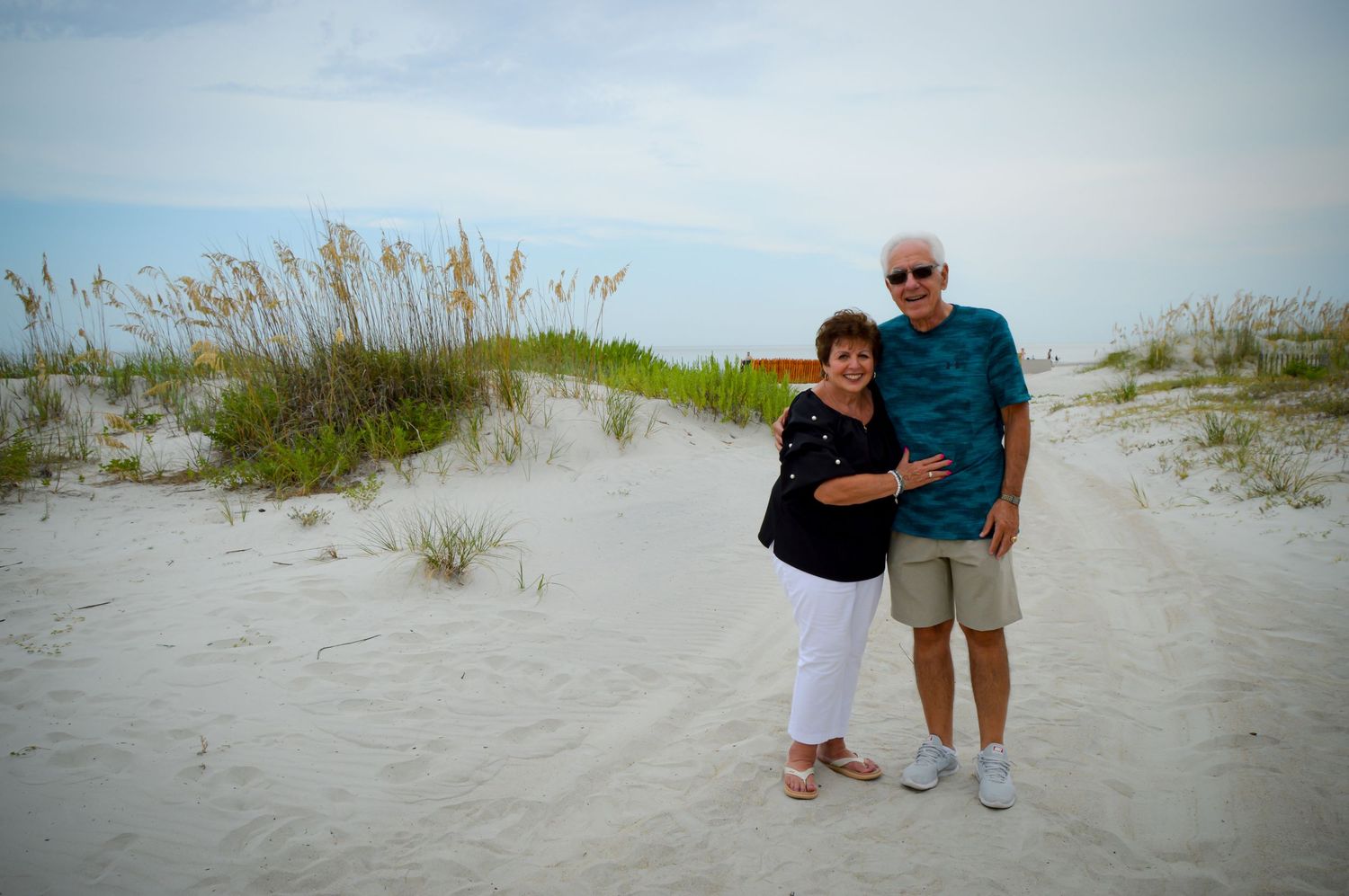 Group walking along a sandy beach path through coastal dunes.