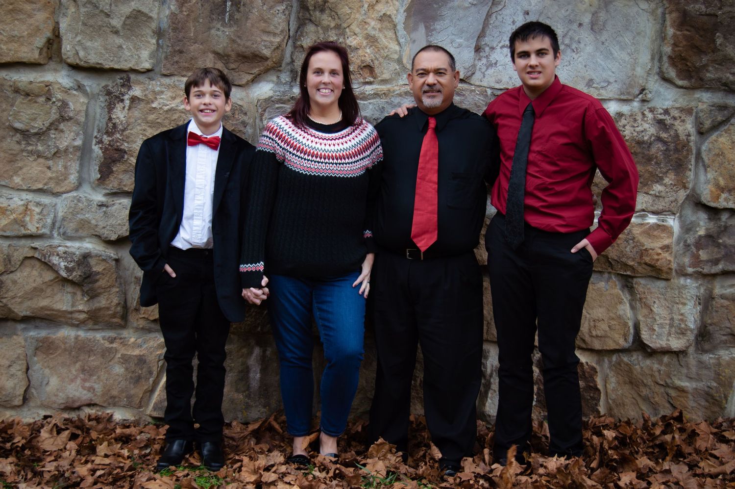 Group photo against stone wall and red barn in casual autumn attire.