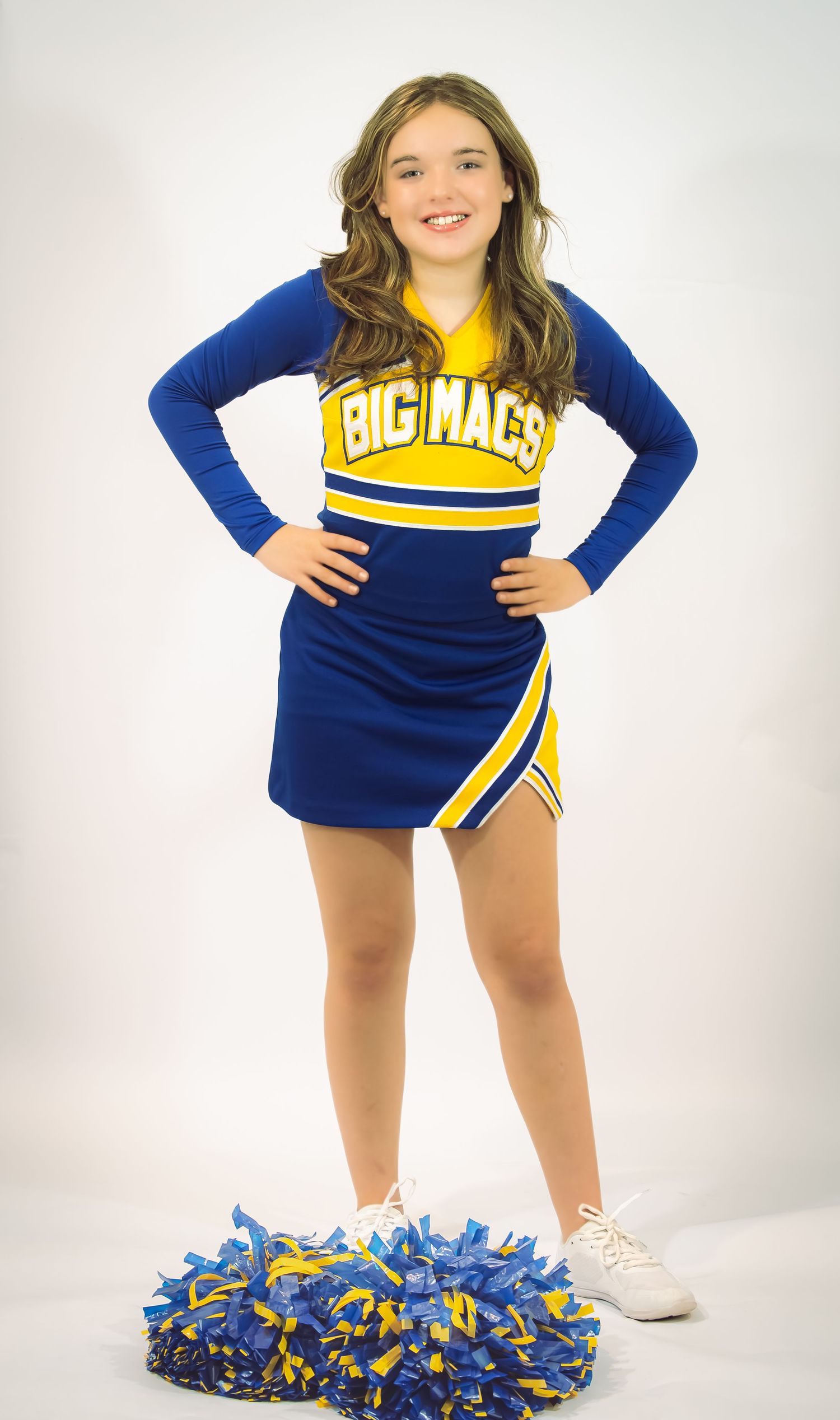 Cheerleader in blue and yellow uniform posing with pom poms against white background.